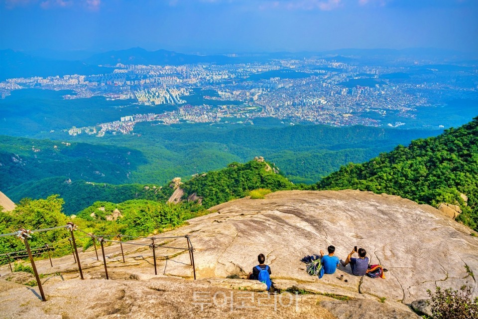 북한산 백운대에 암반 지대에 걸터 앉아 서울의 풍경을 감상하는 등산객
